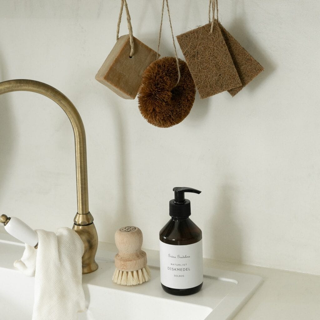 Skrubboll av kokosfiber som hänger i köket tillsammans med andra naturliga rengöringsredskap.