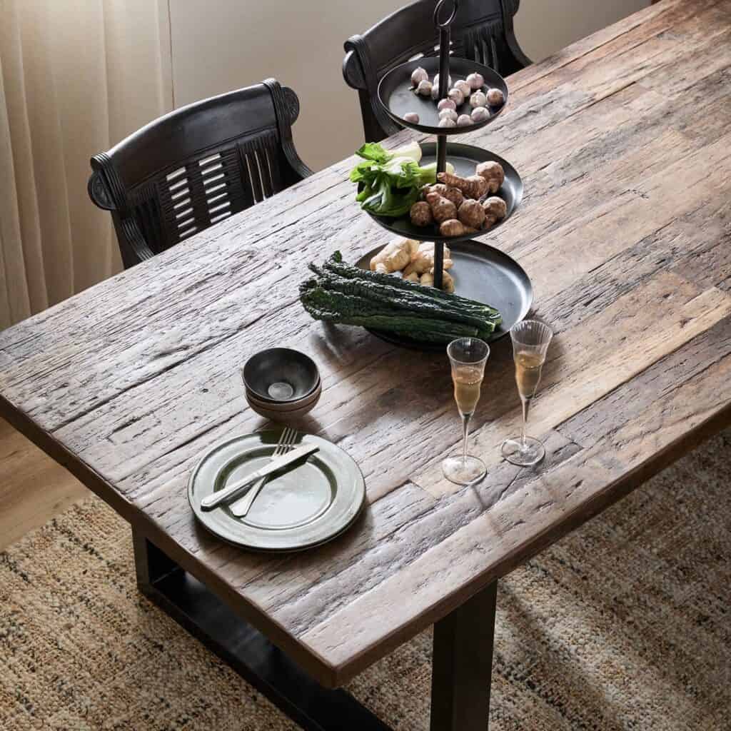 Ett närbild på vintagebordet dekorerat med tallrikar, glas och grönsaker, vilket framhäver träskivans naturliga textur.