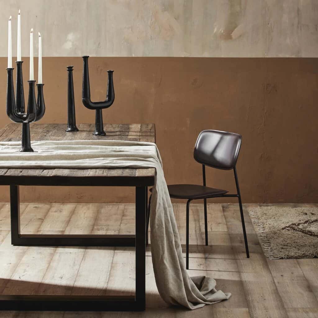 Vintagebord dukat med svarta ljusstakar och en linnefilt, stående i ett modernt vardagsrum med beige väggar och träplankgolv.