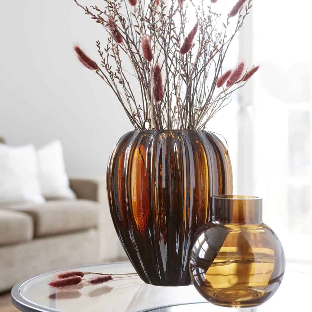 Två glaskrukor, en större och en mindre i bärnstensfärg, med torkade grenar som dekoration.