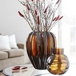 Två glaskrukor, en större och en mindre i bärnstensfärg, med torkade grenar som dekoration.