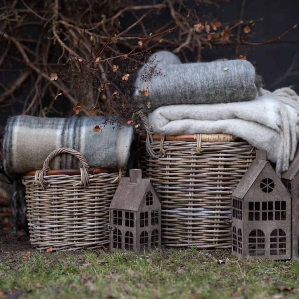 Alexia rottingkorgar dekorerade med filtar och trähus för en rustik utomhusstämning.