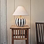 Lampskärm Hedvig i beige linnetyg från Strömshaga placerad på en svart-vit randig lampfot, skapar en mysig och tidlös atmosfär.