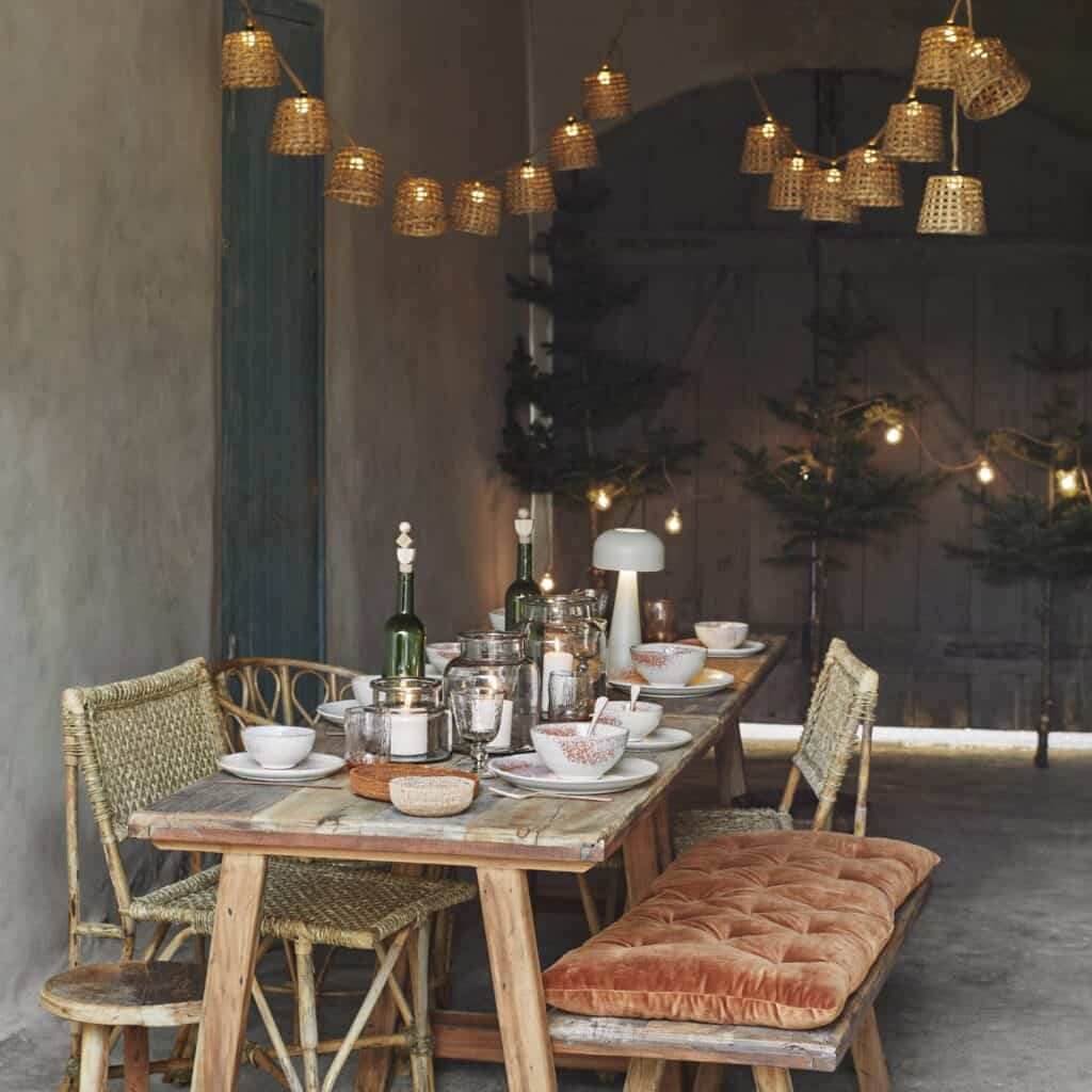 Dukat bord med ljusslinga i bambu från Madam Stoltz som hänger ovanför, skapar en mysig och inbjudande atmosfär i rummet.