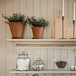 Två Alvaro-krukor med blommor, placerade på en vit hylla i ett rustikt kök med glasburkar.