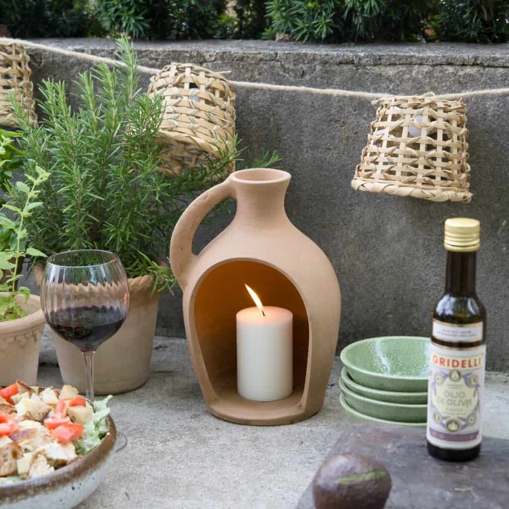 Ljusslinga från Madam Stoltz med små handgjorda lampskärmar i flätad bambu, upphängd utomhus vid en stenvägg, omgiven av terrakottakrukor och levande ljus.