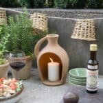 Ljusslinga från Madam Stoltz med små handgjorda lampskärmar i flätad bambu, upphängd utomhus vid en stenvägg, omgiven av terrakottakrukor och levande ljus.