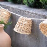 Tänd ljusslinga i handflätad bambu från Madam Stoltz, upphängd mot en stenvägg i kvällsljus, med varm glöd inuti de små skärmarna.