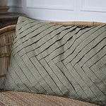 Kuddfodral FERNANDO i olivgrönt bomullstyg med ett elegant diagonalt mönster, placerat på en rottingmöbel.