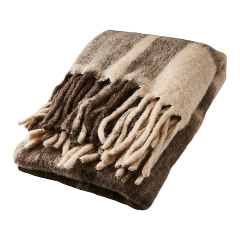 Närbild på FRASSE-filt från Affari of Sweden i färgerna brun, beige och grå med mjuka fransar, hopvikt för att visa den fluffiga texturen.