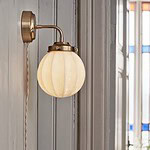 Vägglampan Marit från Strömshaga monterad på en ljusgrå trävägg. Lampans opalglas lyser med ett varmt sken, och den tvinnade beigea sladden syns tydligt.