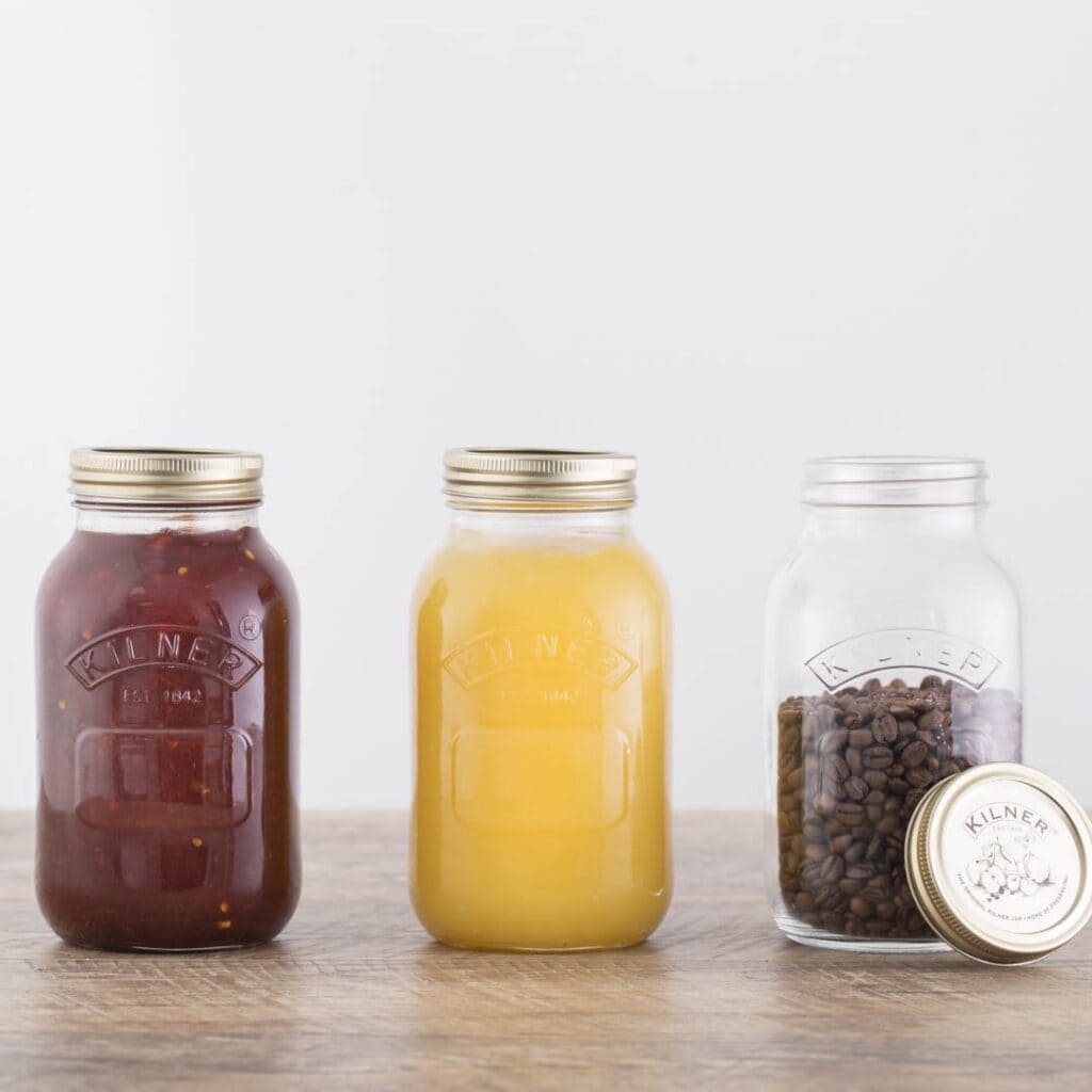Tre Kilner konserveringsburkar fyllda med olika innehåll: tomatsås, äppelmos och kaffebönor, två med skruvlock och en öppen.