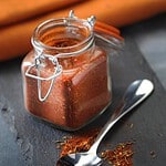 Kilner bygelburk fylld med kryddblandning, står öppen på skärbräda med kryddor och en sked bredvid, redo för användning.