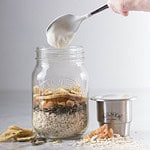 Kilner burk med havre, torkad frukt och frön, tillsammans med en separat metallbehållare för yoghurt eller sås, upplagd för en frukost på språng.