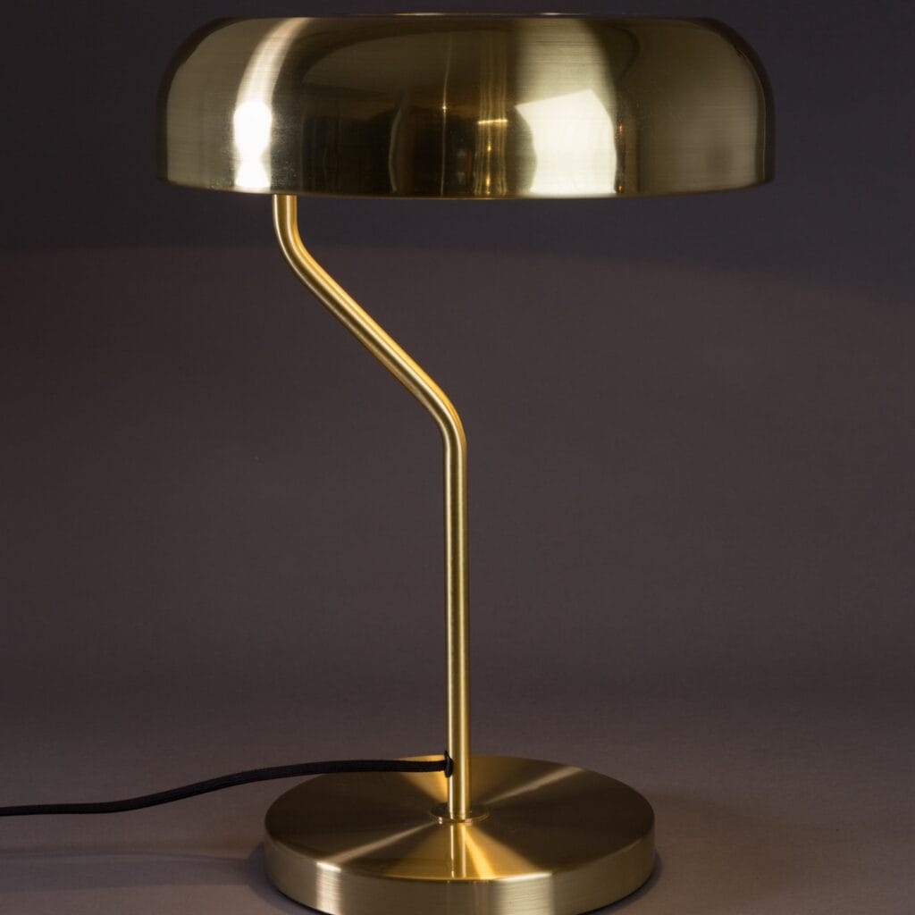 Bordslampa ECLIPSE i mässing från Dutchbone med en modern design och elegant form, fotograferad mot en mörk bakgrund.