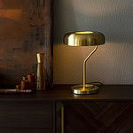 Bordslampa ECLIPSE i mässing från Dutchbone, placerad på en mörk träbyrå med mjukt ljus som skapar en stämningsfull miljö.