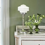 Bordslampa Valter från Strömshaga i förnicklad metall med vit opalglas-kupa, placerad på en vit vintagebyrå mot en grön vägg och dekorerad med gröna glasvaser och blommor.