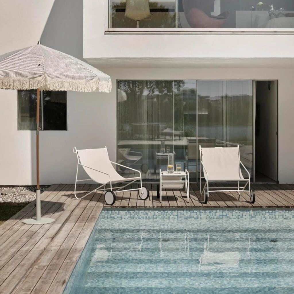 Grårandigt Gatsby parasoll från Brafab vid en pool med vita solstolar och träaltan. Elegant miljö för avkoppling i trädgården.