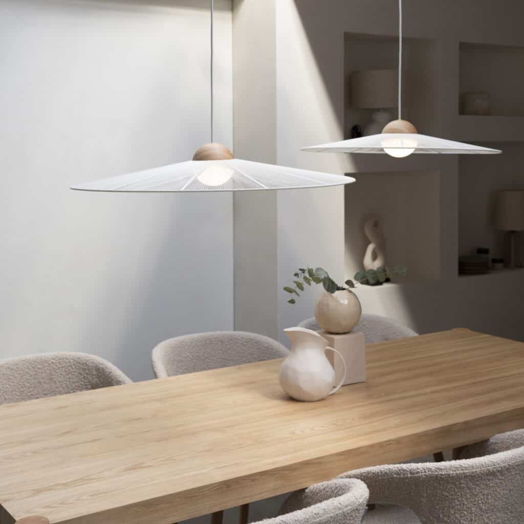 Närbild på två taklampor Belle från Zuiver i beige som hänger över ett ljust träbord i en minimalistisk matsal med neutrala och stilrena detaljer.