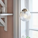 Taklampa Eivor hängande i ett fönster, med räfflad glaskupa som sprider ett behagligt ljus, omgiven av klassiska inredningsdetaljer.