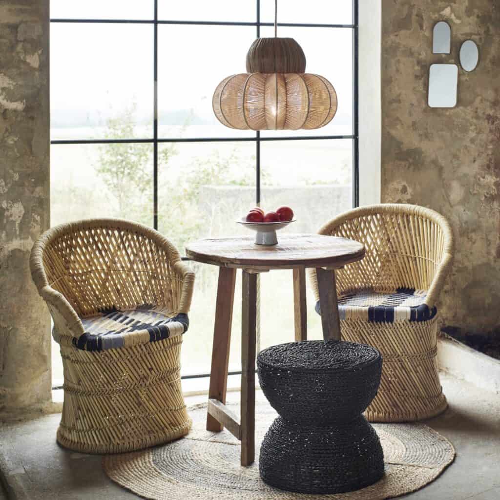 Ett mysigt rum med stora fönster, inrett med en handvävd taklampa i sjögräs och bomullssnöre från Madam Stoltz, omgiven av rottingstolar, ett träbord och en flätad matta.