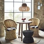 Ett mysigt rum med stora fönster, inrett med en handvävd taklampa i sjögräs och bomullssnöre från Madam Stoltz, omgiven av rottingstolar, ett träbord och en flätad matta.