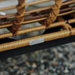 Närbild av Brafab-märket på en loungefåtölj i naturfärgad konstrotting, med detaljerad flätning och svart metallstomme.