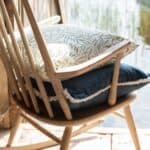 Kuddfodral Fay med grönt bladmönster placerat på en blå kudde i en rustik trästol vid vattnet.