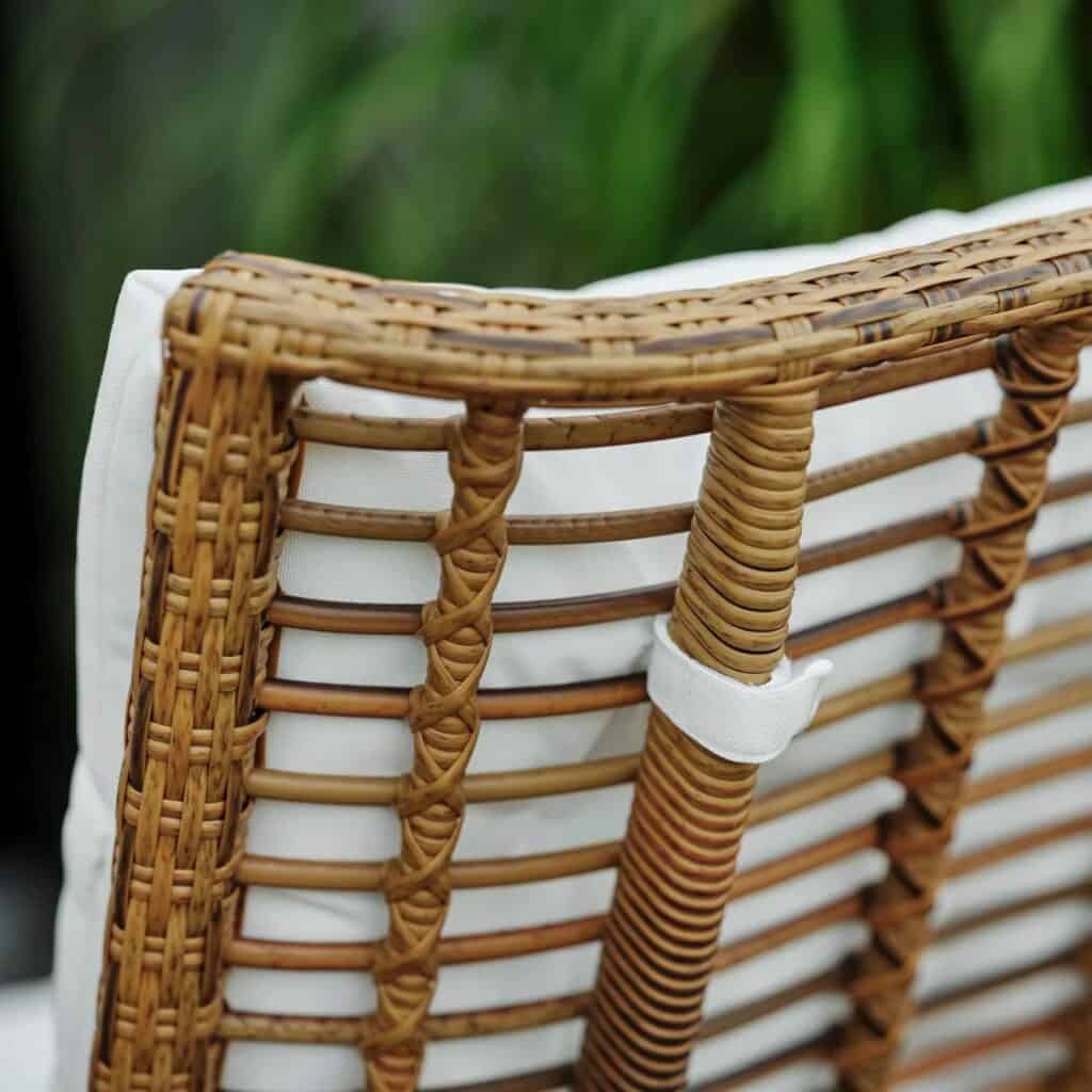 Närbild av baksidan på Covelo loungefåtölj i naturfärgad konstrotting, med detaljerad flätning och vit dyna fäst med ett tygband.