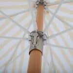 Närbild underifrån på mekanismen och stommen av ett randigt parasoll från Brafab, med robust trästång och vita ribbor som håller duken på plats.