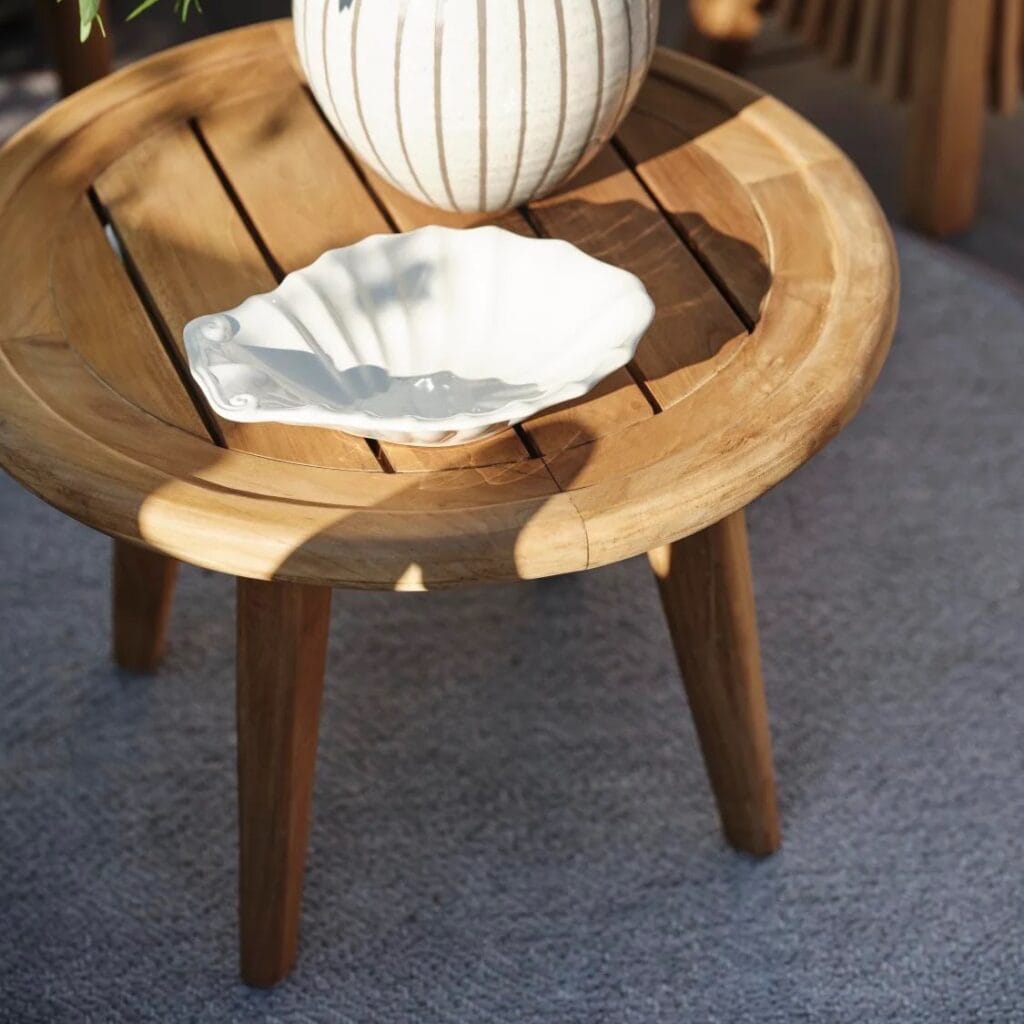 Närbild på sidobord LILJA i teak med en dekorativ keramikskål och vas i naturligt solljus på en uteplats.