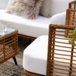 Närbild av Covelo loungesoffa och fåtölj i konstrotting med vita dynor, stilfullt inredd med mjuka kuddar och glasdetaljer.