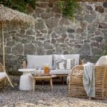 Mysig uteplats med Penzano soffa och fåtölj i naturfärgad konstrotting från Bloomingville. En stilfull loungehörna med mjuka dynor, rustik stenmur och naturnära detaljer.