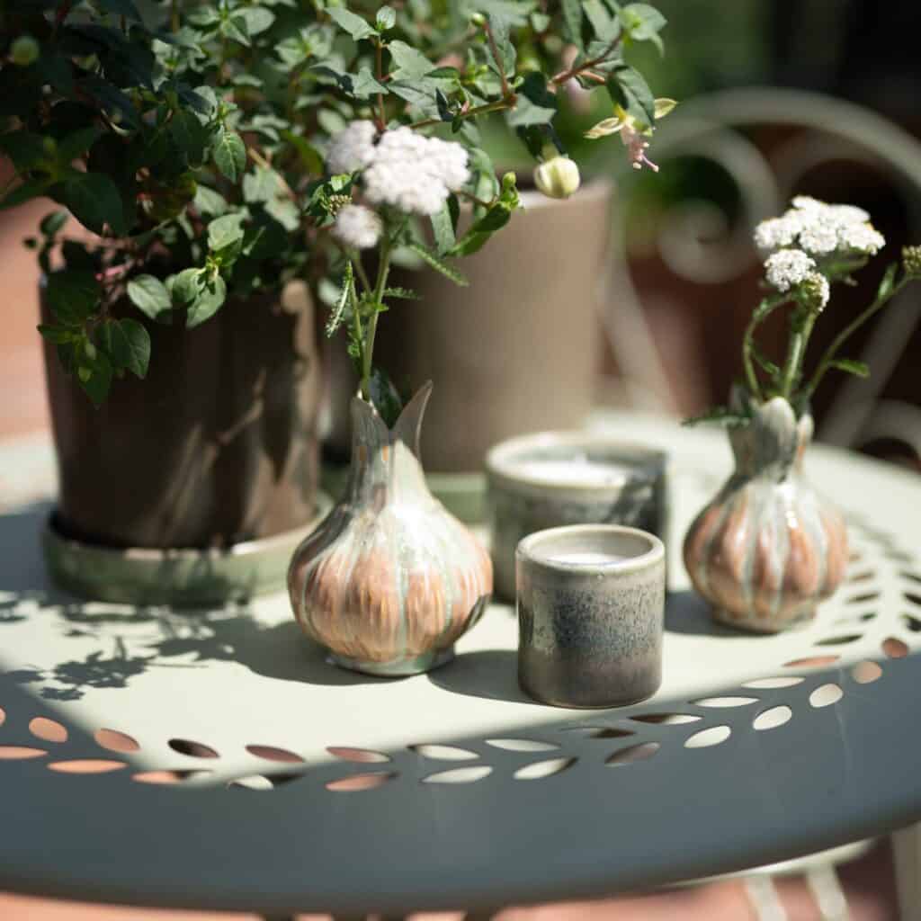 Närbild av ljusgrönt COMO bord från Wikholm Form, dekorerat med keramikvaser, ljuslyktor och blommande växter i en solig trädgårdsmiljö.