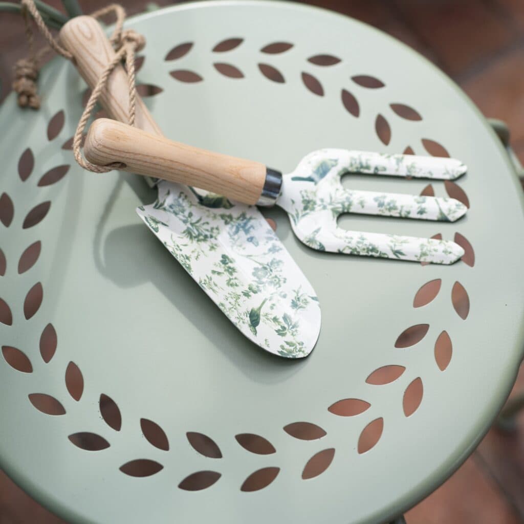 Närbild av ljusgrön trädgårdsstol COMO från Wikholm Form med dekorativt mönstrad sits, prydd med trädgårdsredskap i blommigt mönster och trähandtag.