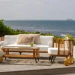 Covelo utemöbel från Brafab – elegant loungegrupp i konstrotting med vita dynor, placerad vid havet på en träaltan, perfekt för uteplats och trädgård.