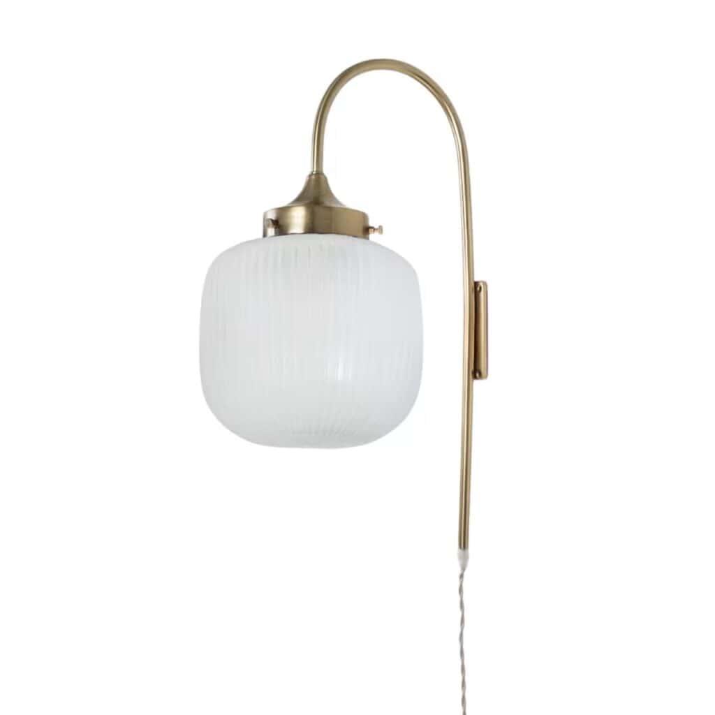 Vägglampa i mässingsfinish med frostat opalglas och rundad design från Strömshaga. Lampan har en beige textilsladd och sprider ett mjukt, varmt ljus. Perfekt för att skapa en mysig atmosfär i hemmet.