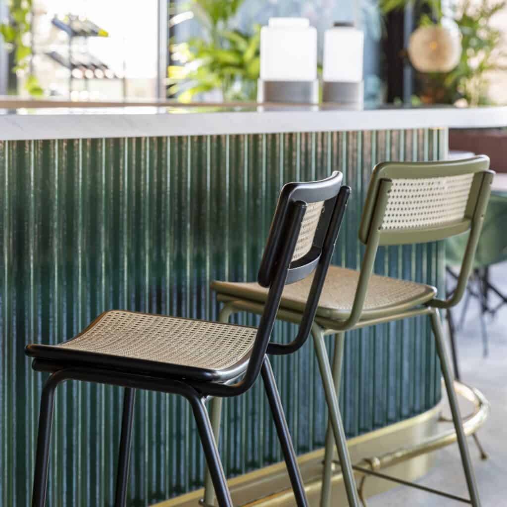 Barstolar JORT från Zuiver i rotting – svart och olivgrön metallram vid marmorbardisk