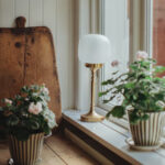 Bordslampa Eli i mässing med frostat glas placerad i ett fönster
