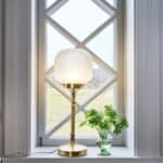 Bordslampa med frostat glas och mässingsfot – Strömshaga Eli i fönster med grön växt