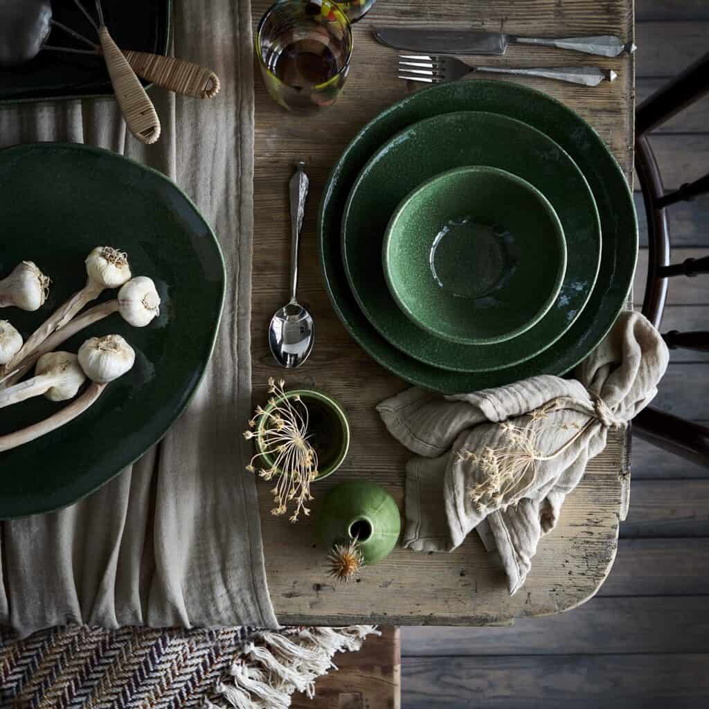 Rustik dukning med ELSA bordduk i beige, kombinerad med gröna tallrikar och naturnära detaljer.