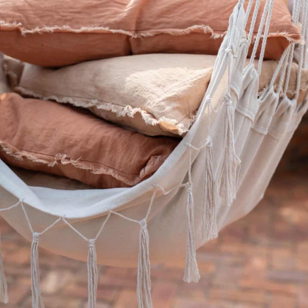 Närbild av hängstolen ARMIDA i offwhite från Wikholm Form, dekorerad med mjuka kuddar i jordnära toner och vackra fransdetaljer.