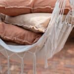 Närbild av hängstolen ARMIDA i offwhite från Wikholm Form, dekorerad med mjuka kuddar i jordnära toner och vackra fransdetaljer.