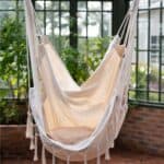 Hängstol ARMIDA i offwhite från Wikholm Form, upphängd i ett ljust och grönskande växthus. En stilren och bohemisk sittplats för avkoppling.