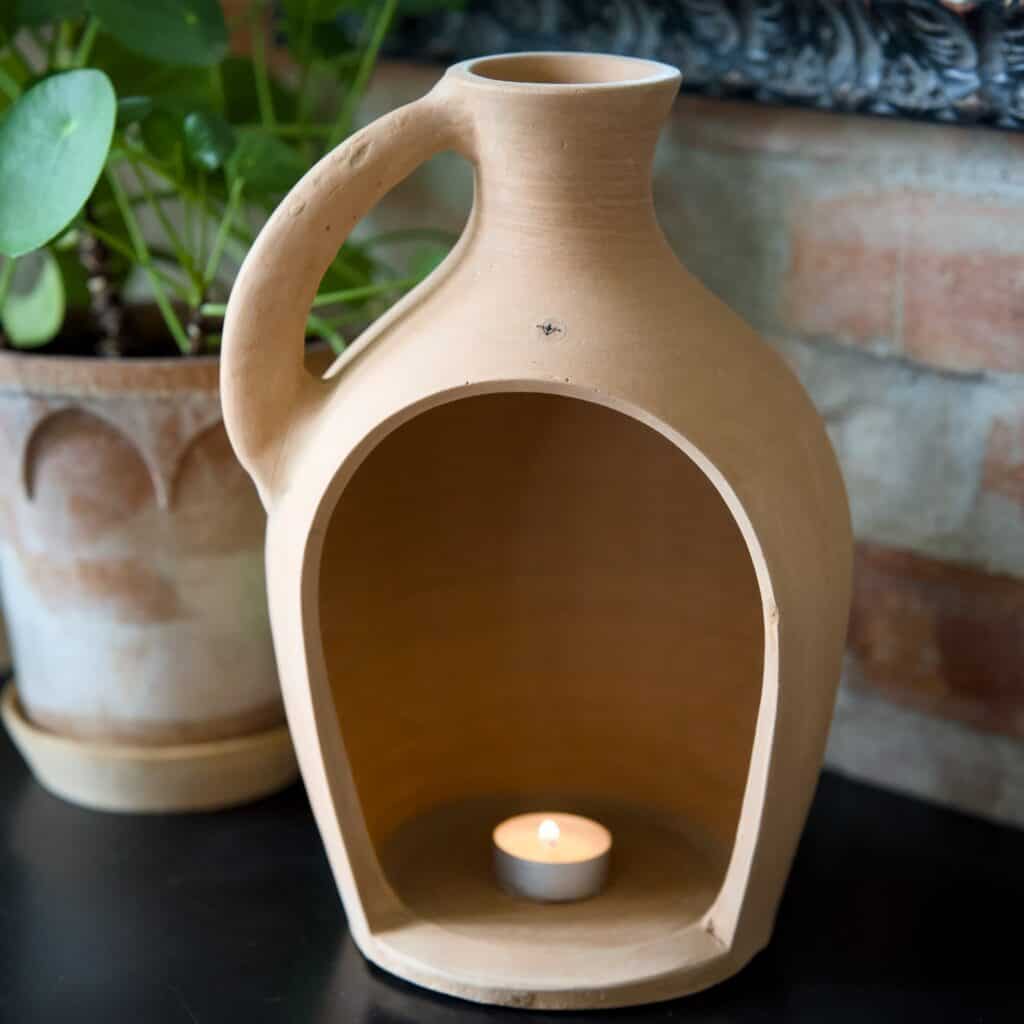 Floda Lykta i terrakotta från Affari of Sweden med ett värmeljus inuti, placerad på ett bord med gröna växter i bakgrunden.