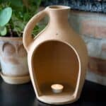 Floda Lykta i terrakotta från Affari of Sweden med ett värmeljus inuti, placerad på ett bord med gröna växter i bakgrunden.