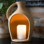 Floda Lykta i terrakotta från Affari of Sweden med ett tänt blockljus inuti, sprider ett varmt och stämningsfullt sken i en rustik miljö.