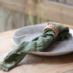 TAKI servett i grön linneblandning med franskant, elegant rullad i en naturnära servettring på en rustik dukning.