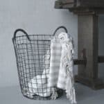 Amarlin trådkorg i svart järn från Wikholm Form med randig pläd, placerad intill ett rustikt träbord