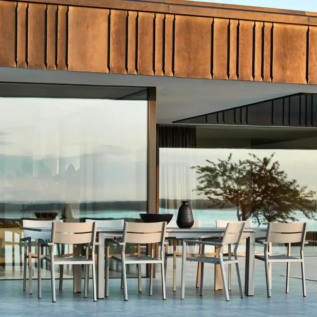 Karmstolar DELIA i khaki runt ett rektangulärt utebord i eftermiddagssol.